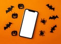 Mockup, smartphone, paper black bats, spiders and pumpkins on orange background. Halloween background Royalty Free Stock Photo