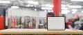 Mockup space on wooden tabletop with blank screen tablet mockup over blurred fitness gym, 3d rendering