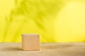 Mockup. Textured cube of beige surface on a yellow background with shadows from plants