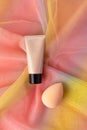 Mockup tonal CC or BB cream foundation makeup and beauty blender sponge on colorful rainbow organza fabric. Cosmetic