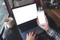 Mockup top view image of business woman holding white mobile phone with blank screen with laptop and coffee cup on wooden table