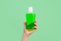 Mockup of unbranded bottle with green liquid for branding and label and male hand on green background. Mouthwash or teeth care