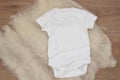 Mockup of white baby bodysuit on wood background. Blank baby clothes template mock up. Flat lay styled stock photo