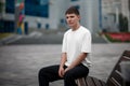 Mockup of a white t-shirt on a young guy sitting on a bench on a blurred background in the park  stylish clothes for presentation Royalty Free Stock Photo