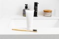 Mockup white tube of toothpaste and natural wooden toothbrush standing on sink on faucet background. Concept of organic oral care