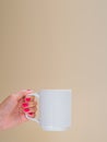 Mockup woman with red manicure holds white ceramic cup isolated on beige. Copy space for your text Royalty Free Stock Photo