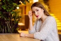 Model with blonde long hair and bright pink lipstick in white sweater sitting on a chair in a cafe with beautiful stylish interior Royalty Free Stock Photo