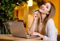 Model with blonde long hair and bright pink lipstick in white sweater sitting on a chair in a cafe with beautiful stylish interior Royalty Free Stock Photo