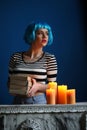 Model in blue wig posing with books and candles. Close up. Dark background