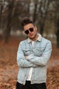 Model cool American young man in fashionable sunglasses in a stylish denim jacket with a trendy hairstyle in the park. Handsome Royalty Free Stock Photo