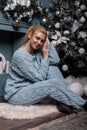 Model of a cute young woman in a stylish knitted blue suit posing on the floor near a beautiful Christmas tree with vintage toys. Royalty Free Stock Photo