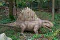 Model of dinosaur dimetrodon from genus nonmammalian synapsids, standing on four legs on grass, on background of trees, side view