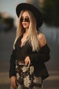 Model girl with blond hair wearing sunglasses and trendy hat walking alone in the city street Royalty Free Stock Photo