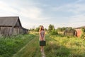 A model girl in a retro dress is holding in her hands a vintage suitcase on an abandoned country road overgrown with grass Royalty Free Stock Photo