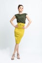 Model in green blouse, yellow suede skirt with yellow belt, white heeled sandals isolated on white background.