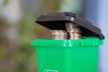 A model of a green trash can with dollar coins coming out of the lid