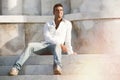 Model handsome man relaxed sitting on the steps of white marble. Royalty Free Stock Photo