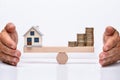 Model Home And Coins Balancing On Wooden Weighing Scale