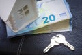 The model of the house, a bundle of money worth 20 euros and the keys to the future home lie on a white plate Royalty Free Stock Photo