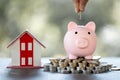 Model of house with female hand putting coin in piggy bank on blurred background. Money saving or investing for home loan or real Royalty Free Stock Photo