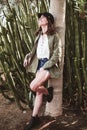 Model laughing with black cap resting on the trunk of a tree near cactus