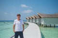 Model man in fashionable white t-shirt and black shorts at over water villas at tropical island luxury resort Royalty Free Stock Photo