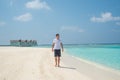 Model man wearing white t-shirt and black shorts walking on the tropical beach at the island luxury resort