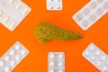 Model of pancreas gland surrounded by six blister packs with white pills on orange background. Photo concept art of treatment or