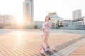 Model in pink dress and pink kick scooter pose against the background of the city landscape in the sunset and smiles Royalty Free Stock Photo