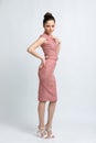 Model in pink suede dress with belt, white sandals, with silver chain around the neck, on white background.