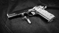 Model 1911 pistol and three cartridges (.45 ACP) on a black denim background, monochrome photo