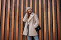 Model of a positive young woman with a beautiful smile in fashionable outerwear in a knitted stylish hat with a leather handbag Royalty Free Stock Photo