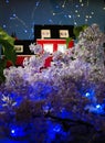 Model of a red brick house in a thicket of lilacs with illumination from a led garland