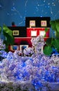 Model of a red brick house in a thicket of lilacs with illumination from a led garland