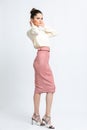 Model in shirt of milk color, pink suede skirt with belt, white heeled sandals isolated on white background.