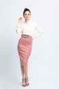 Model in shirt of milk color, pink suede skirt with belt, white heeled sandals on white background.