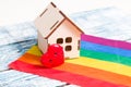 A model of a small wooden house and a heart stand on the flag of the colors of the rainbow