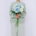 Model Standing In white Room with Flowers In Her Hands. Fresh aqua menthe colours trends. Spring summer collection