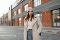 Model of a trendy young woman in fashionable youth outerwear in a knitted stylish hat with a leather handbag posing near a vintage Royalty Free Stock Photo