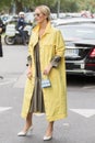 Model wearing a pair of shiny white shoes with heels, a yellow overcoat and a tiny blue handbag Royalty Free Stock Photo