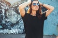 Model wearing plain tshirt and sunglasses posing over street wall