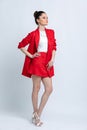 Model in white blouse, red skirt and jacket and white sandals with silver chain and pendant on neck, on white background.