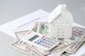 Model white house on pile of dollar money, calculator and contract documents on grey background
