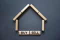 Model of a wooden house from wooden blocks. Words `buy sell`. Copy space. Business concept. Beautiful grey background Royalty Free Stock Photo