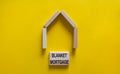 Model of a wooden house. Words `blanket mortgage` on wooden blocks. Copy space. Business concept. Beautiful yelllow background Royalty Free Stock Photo