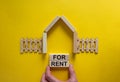 Model of a wooden house. Words `for rent` on wooden blocks. Male hand, wooden fence. Copy space. Business concept. Beautiful Royalty Free Stock Photo