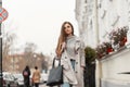 Model of a young brown-haired woman in a fashion trench coat in a stylish knitted sweater with a leather black bag walks on the Royalty Free Stock Photo