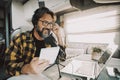 Modern adult man wokring with laptop and microphone inside a camper van in digital nomad job lifestyle. Technology and travel.