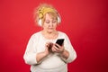 A modern aged woman looks at her smartphone and at the same time listens through headphones Royalty Free Stock Photo