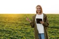 Modern agribusiness. Female farmer holds digital tablet and soya plant in hand in field, examines, checks, Smart farming